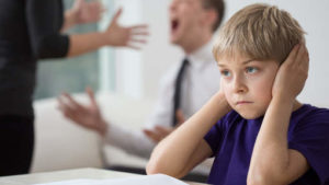 image de l'article : enfants victimes de violences conjugales. cette image représente un enfant qui se bouche les oreilles avec ses mains devant ses parents qui se crient dessus.